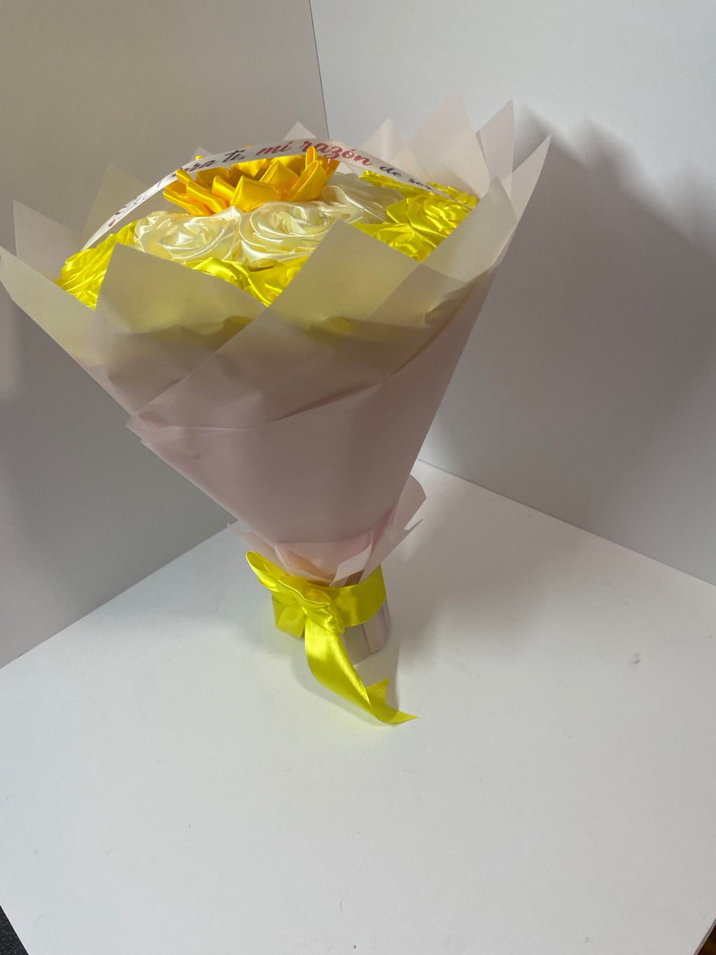 Side view of golden yellow and ivory satin rose and sunflower bouquet wrapped in soft blush paper