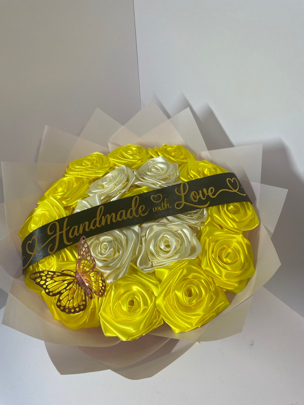 Angled view of golden yellow and ivory satin rose bouquet with butterfly and blush wrapping paper