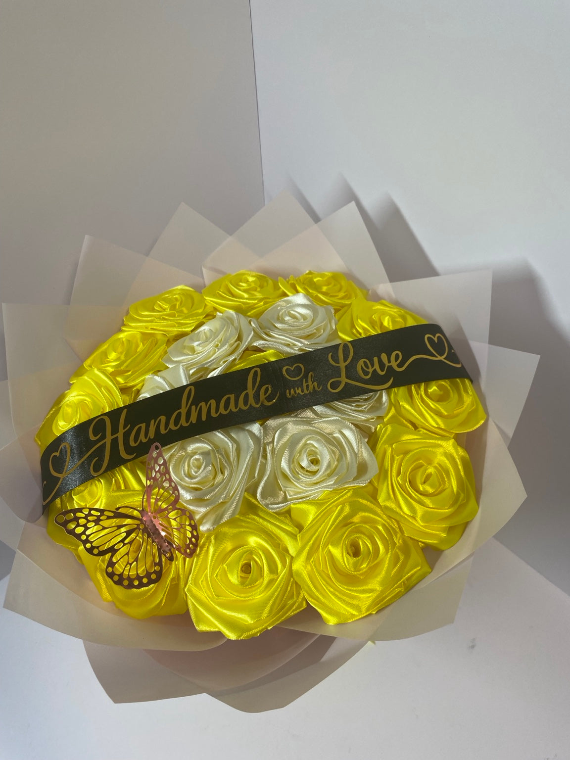 Angled view of golden yellow and ivory satin rose bouquet with butterfly and blush wrapping paper