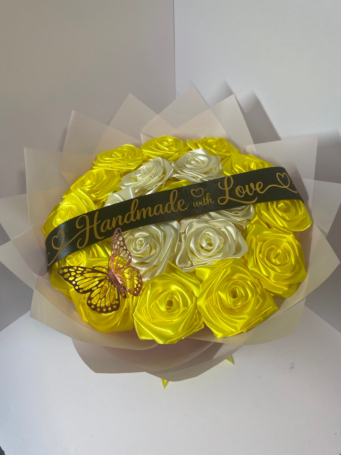 Close-up of golden yellow and ivory satin roses with pink butterfly and black Handmade with Love ribbon