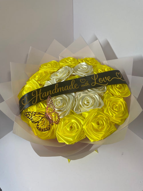 Close-up of golden yellow and ivory satin roses with pink butterfly and black Handmade with Love ribbon