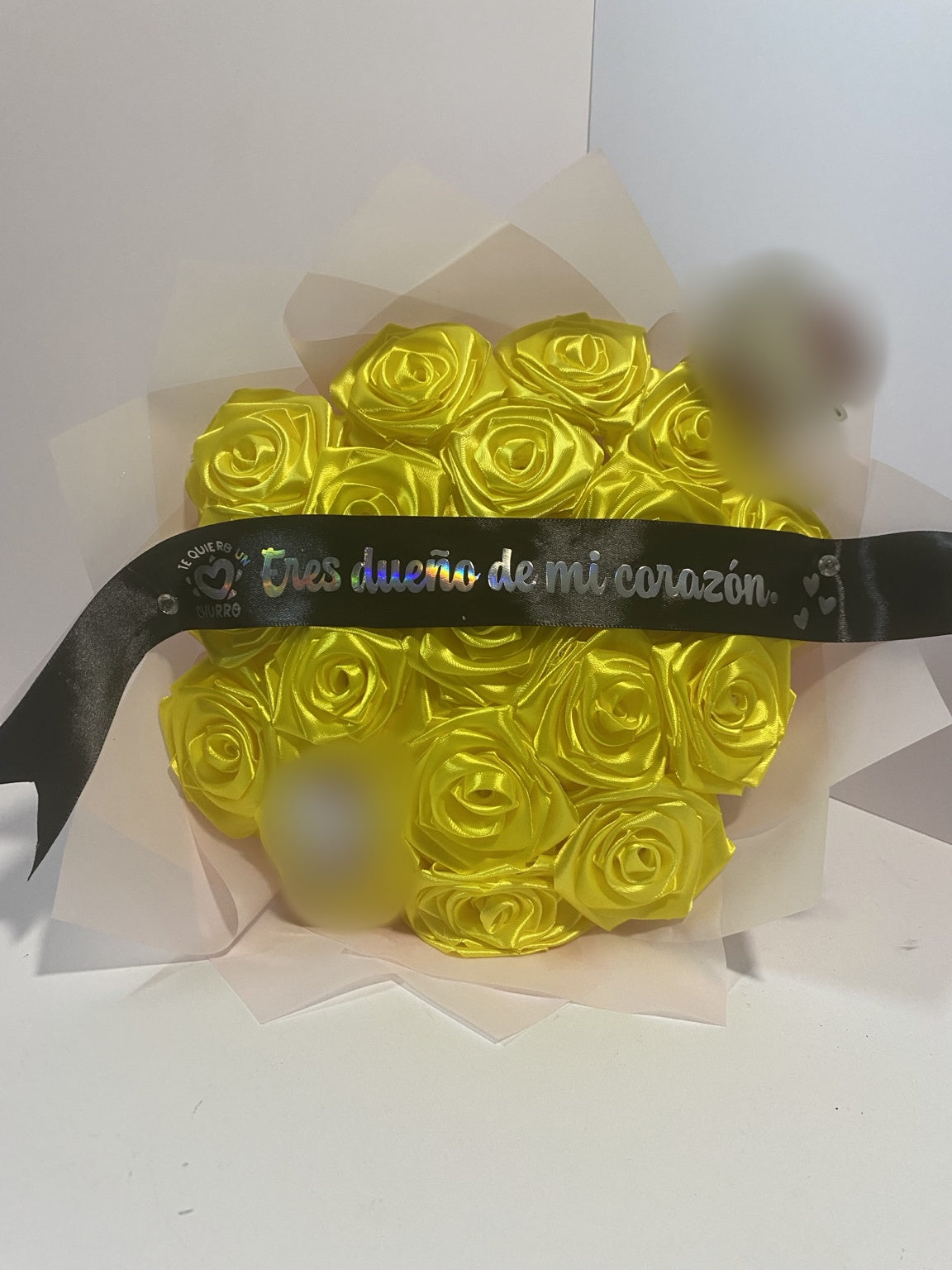 Close-up of golden yellow satin roses with blurred character accents and a black Spanish message ribbon
