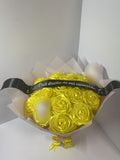 Golden yellow satin rose bouquet with blurred character decorations, black message ribbon, and soft blush wrapping paper