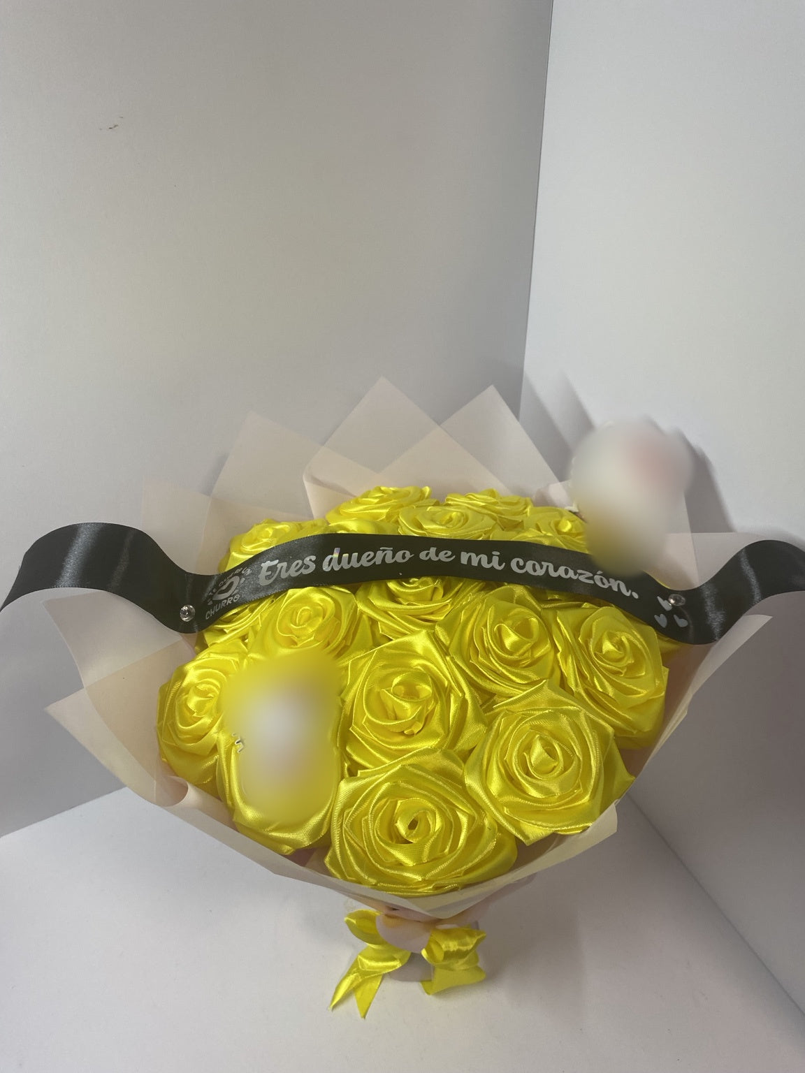 Golden yellow satin rose bouquet with blurred character decorations, black message ribbon, and soft blush wrapping paper