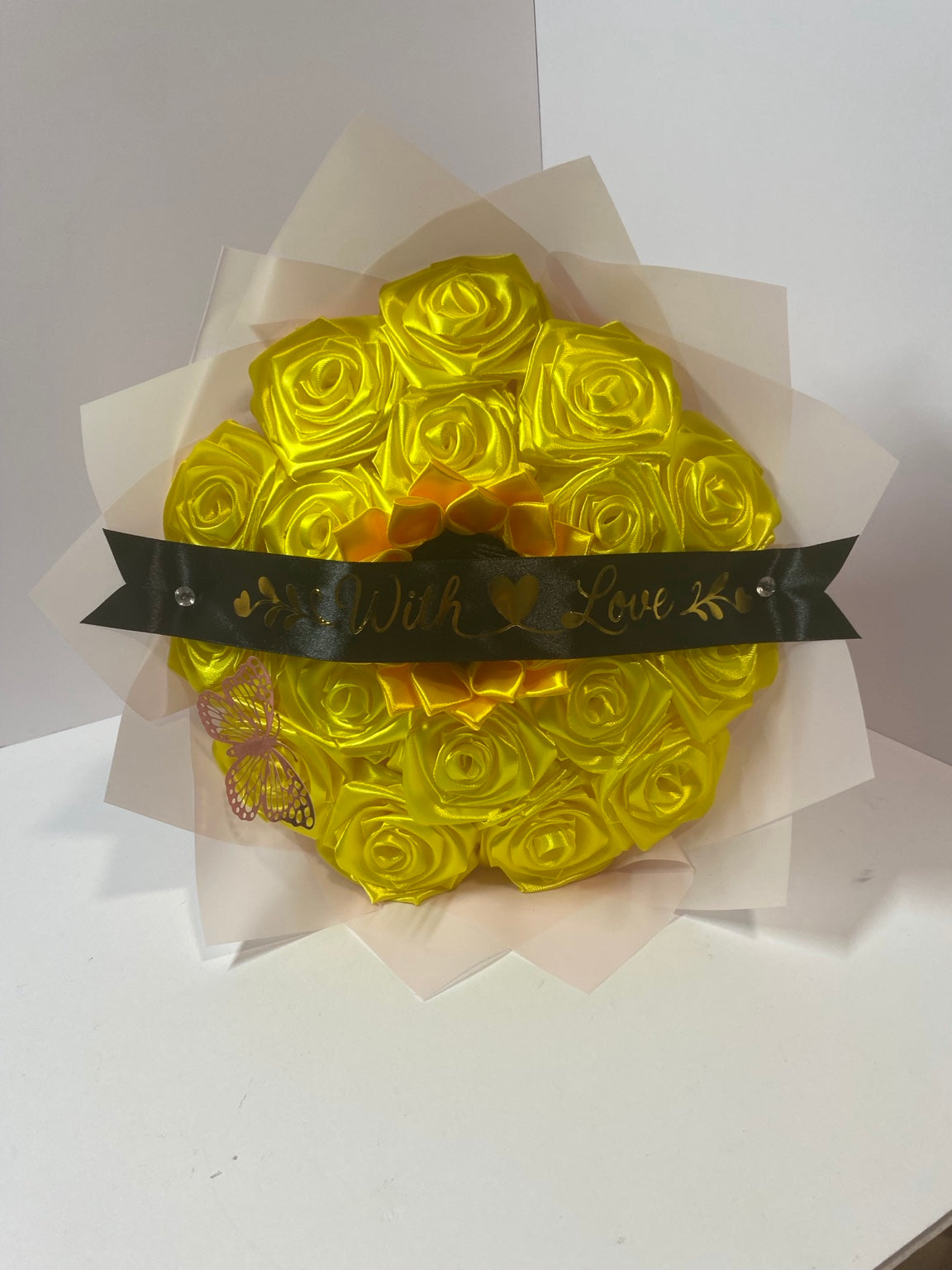 Front detail of golden satin rose and sunflower bouquet with black With Love ribbon and blush wrapping paper